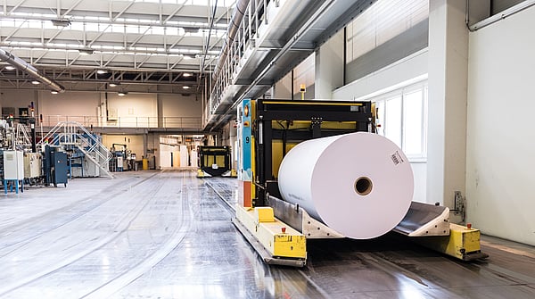 a reel of white packaging paper attached to a machine on a factory floor